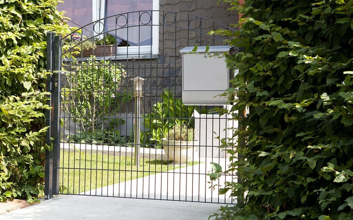 Einflügeliges Gartentor aus Metall mit schlichten Stabdesign, seitlich von Hecken umgeben