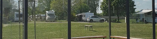 Freistehende Wartehalle aus dunklem Stahl mit Glasseitenwänden, Flachdach und Sitzbänken auf gepflastertem Untergrund