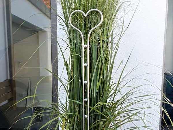 Gartenstab aus Edelstahl mit Herzform vor Ziergras im modernen Außenbereich