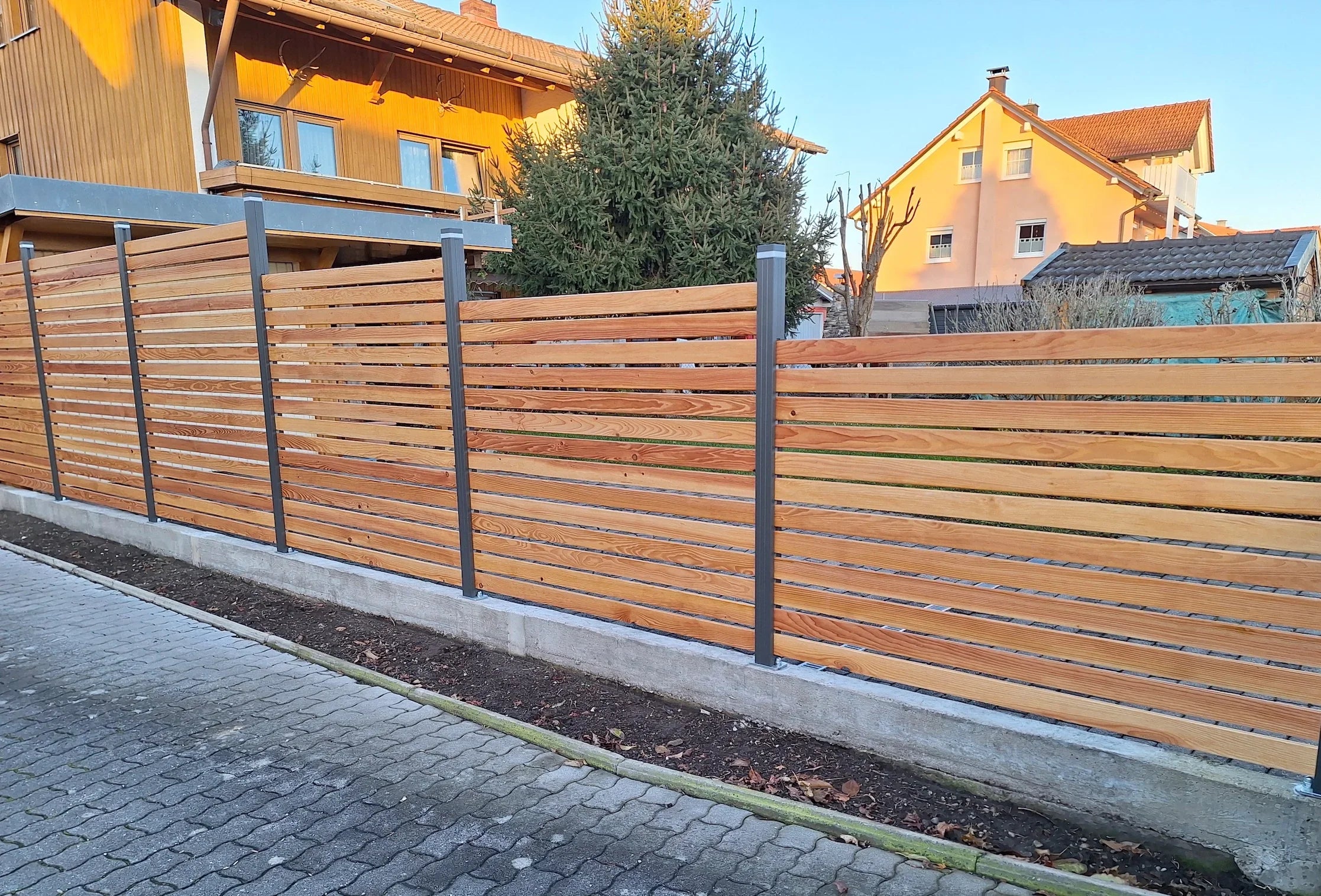 Moderner Sichtschutzzaun aus Holz mit Alu-Pfosten vor Wohnhäusern im Garten
