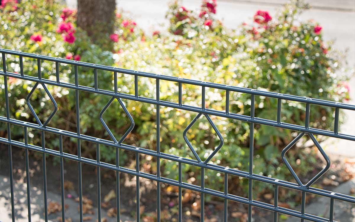 Doppelstabmattenzaun Modell GIRONA mit Rautenmuster vor blühendem Garten