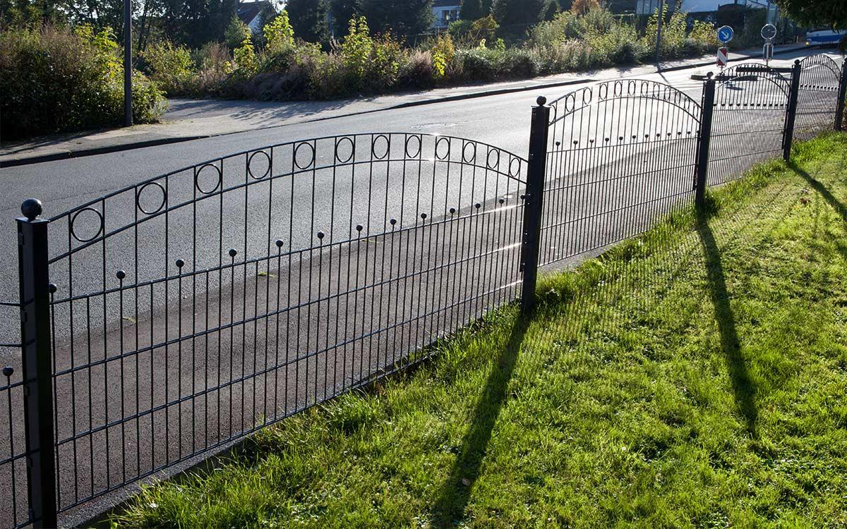 Doppelstabmattenzaun Modell WIEN aus Metall mit dekorativen Bögen und Kreisen an einer Straße.
