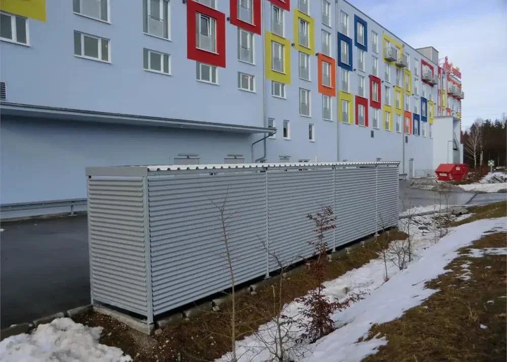 Moderne Fahrradüberdachung aus Metall vor einem bunten Wohngebäude im Winter