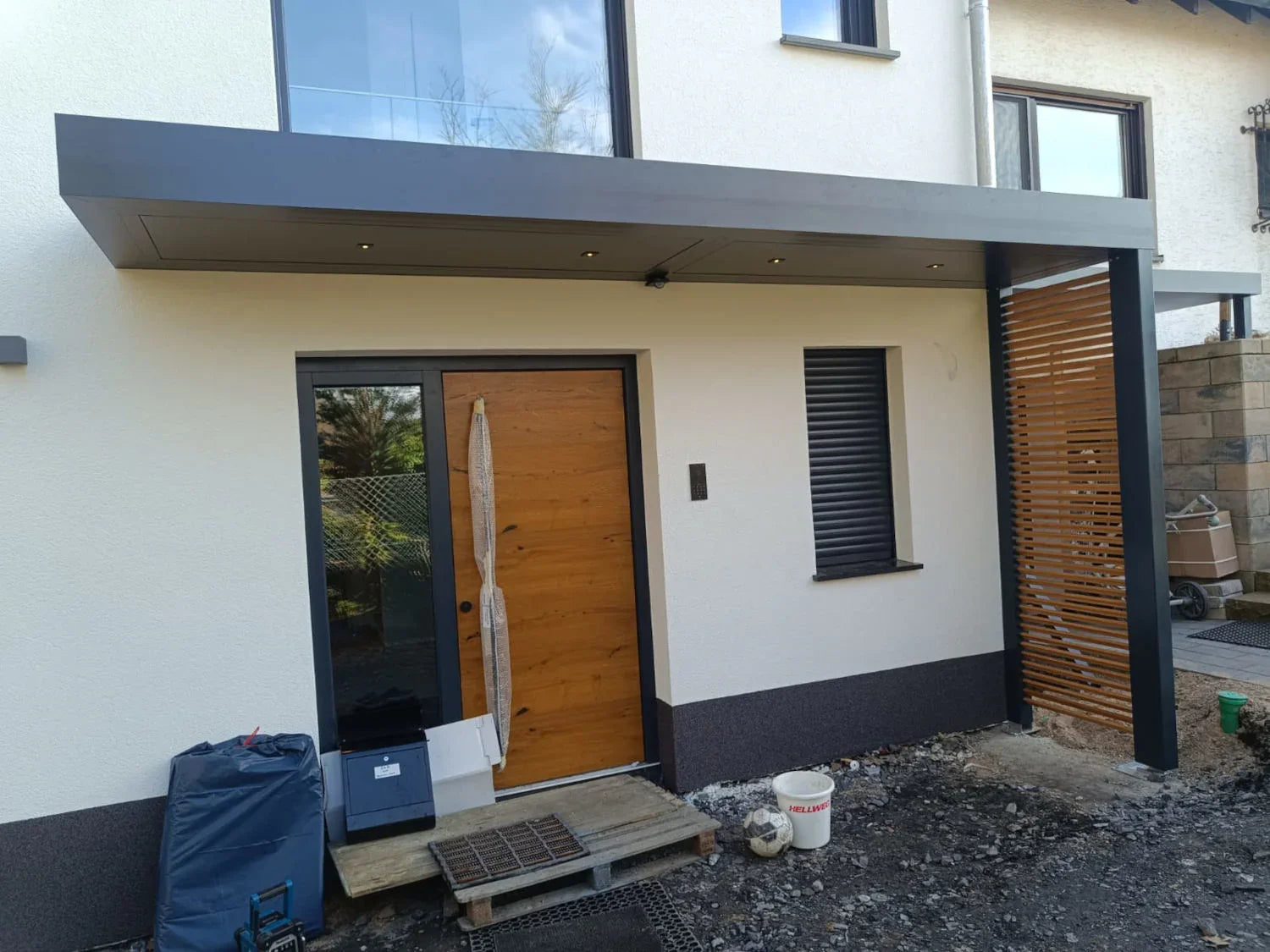 Moderne Metallüberdachung mit LED-Beleuchtung über Hauseingang, seitliche Lamellenwand, Holzhaustür