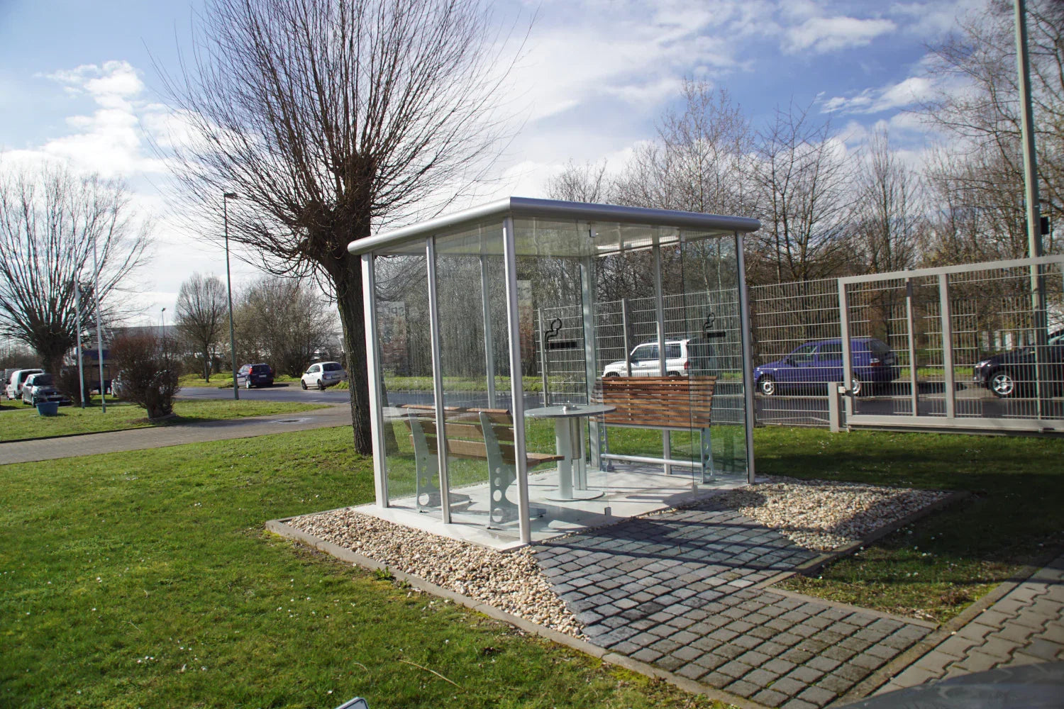 Modernes, verglastes Raucherunterstand mit Sitzbänken aus Metall und Holz im Außenbereich
