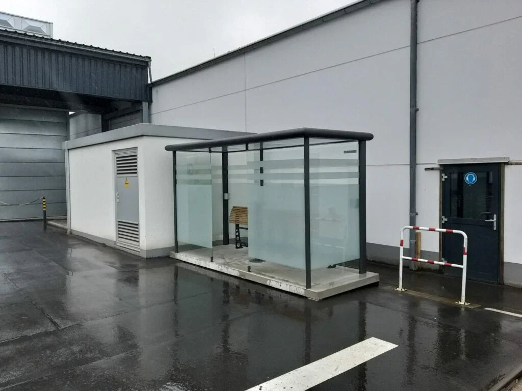 Raucherkabine aus Glas und Metall im Industriebereich auf nassem Außengelände