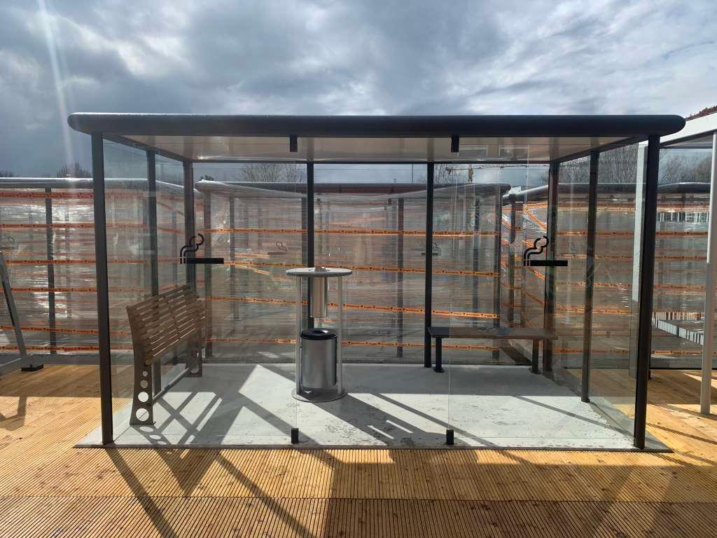 Raucherkabine aus Glas mit Sitzbank und Aschenbecher auf Außenterrasse