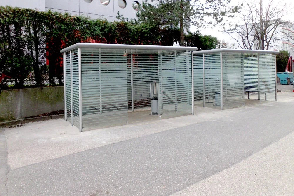 Moderne Raucherkabine aus Metall und Glas im Außenbereich, mit Aschenbecher ausgestattet