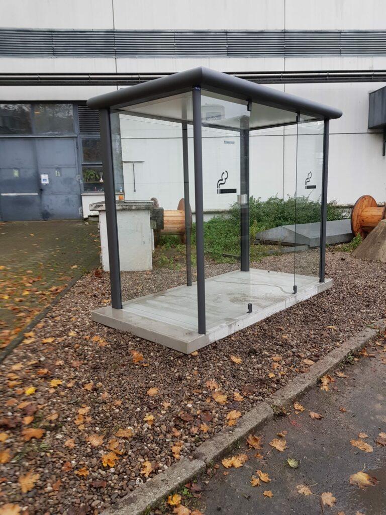 Raucherkabine aus Glas und Metall für den Außenbereich vor einem Firmengebäude
