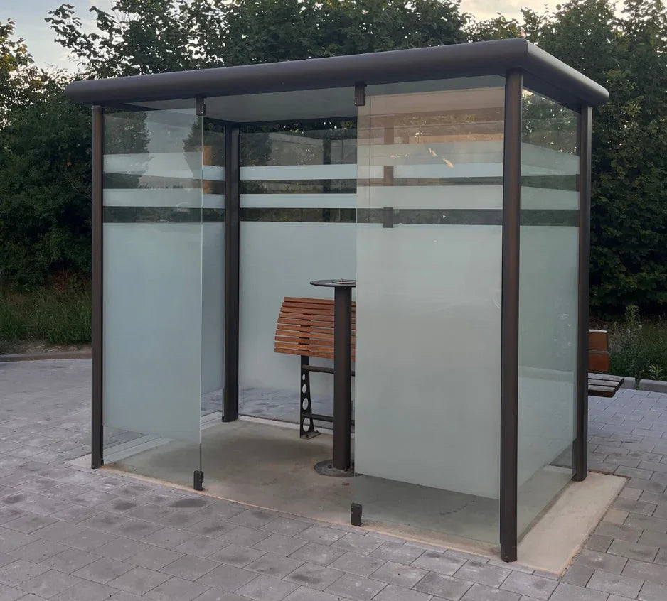 Raucherunterstand aus Aluminium und Glas mit Bank auf gepflastertem Außenbereich
