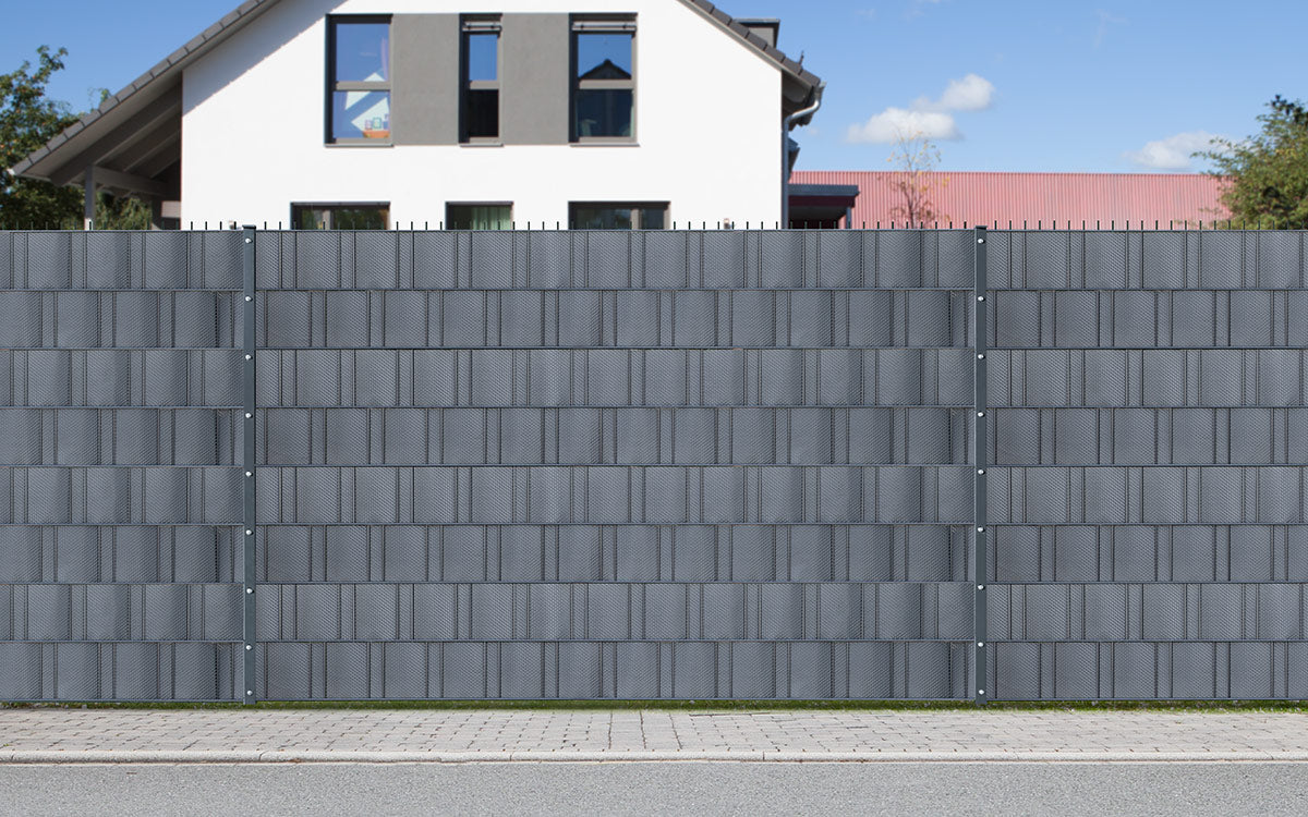 Blickdichter Zaun mit cube-Sichtschutz und Einfahrtstor entlang einer Straße