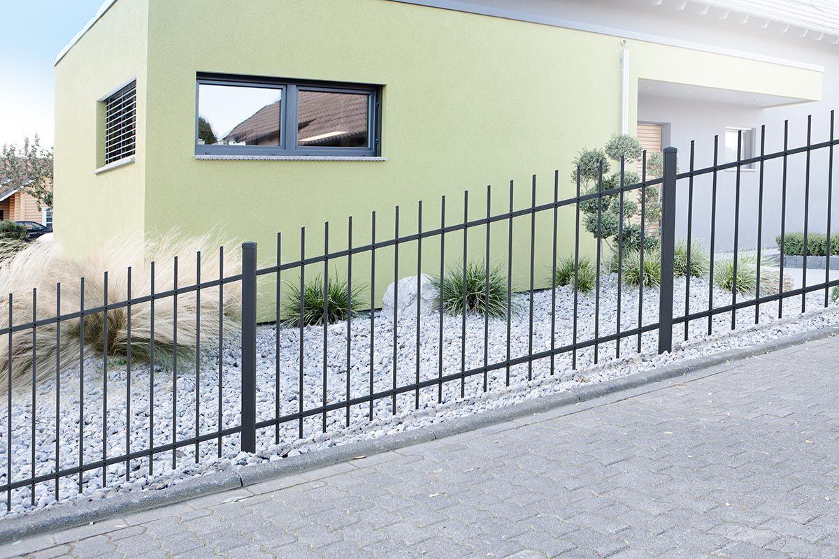 Moderner Steigungszaun aus Metall vor Haus mit Kies und Ziergräsern im Garten