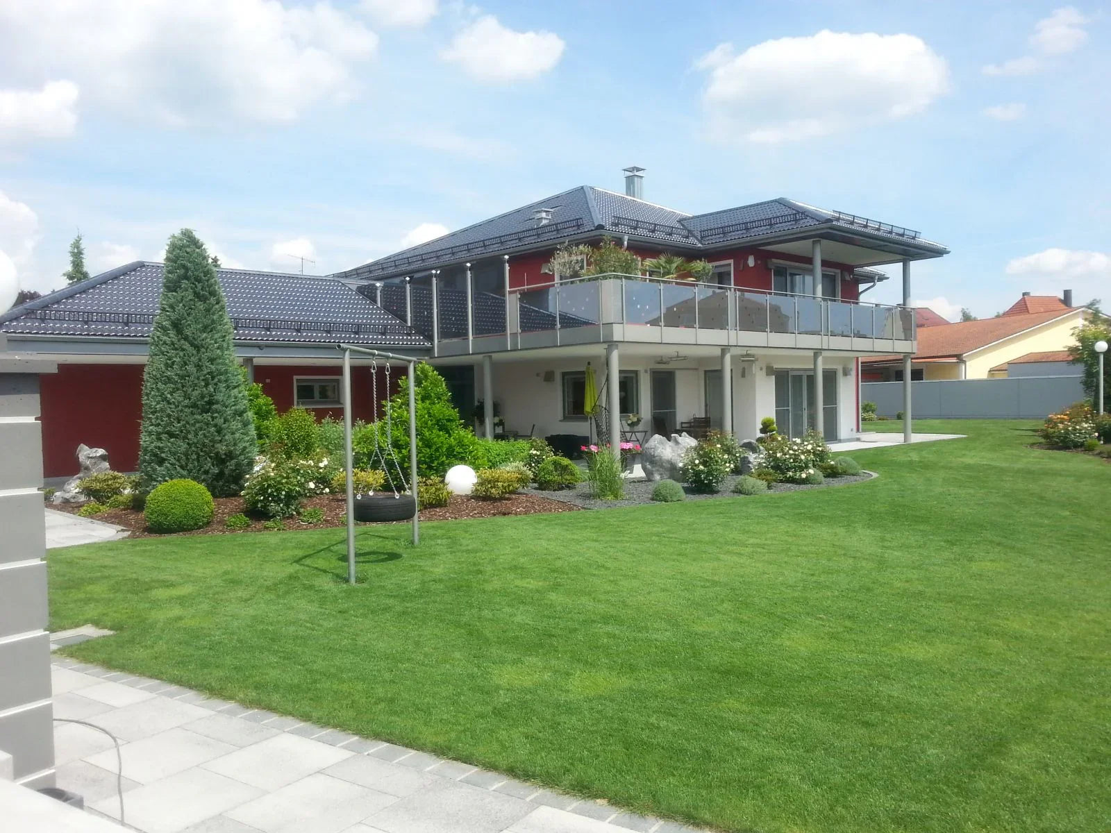 Modernes Haus mit großem Garten und Glas-Balkongeländer aus Metall, sonniger Tag