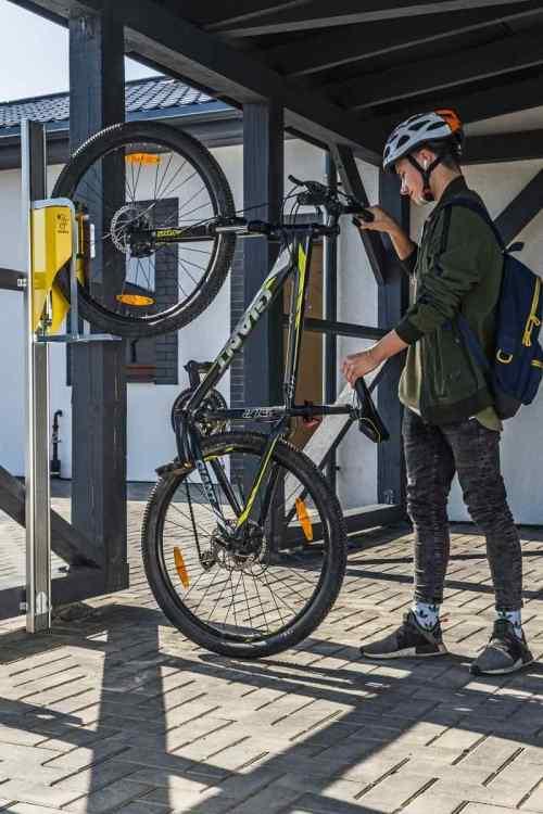 Fahrrad an vertikaler Wandhalterung im Außenbereich, Person mit Helm bedient Fahrradlift