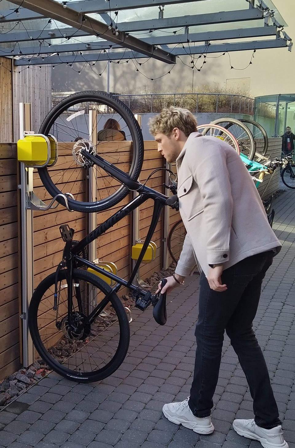 Mann nutzt vertikale Fahrrad-Wandhalterung mit automatischem Fahrradlift im Außenbereich.