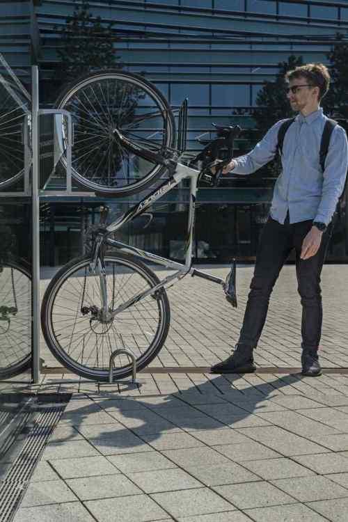 Mann stellt Fahrrad mit vertikaler Fahrrad-Wandhalterung draußen an Glasfassade ab