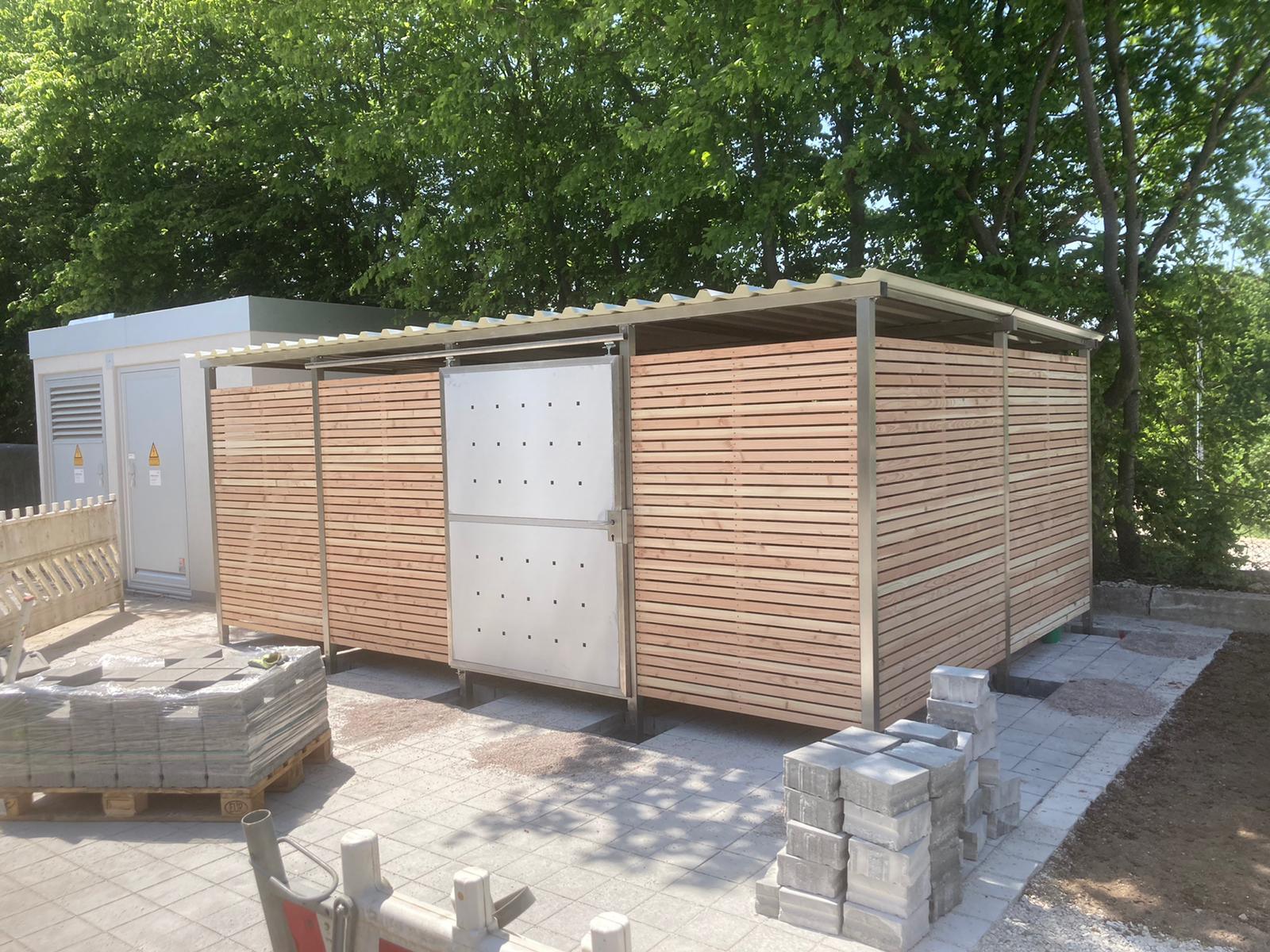 Großes Mülltonnenhaus und Gerätehaus aus Holz und Metall auf gepflastertem Hof, bei Tageslicht