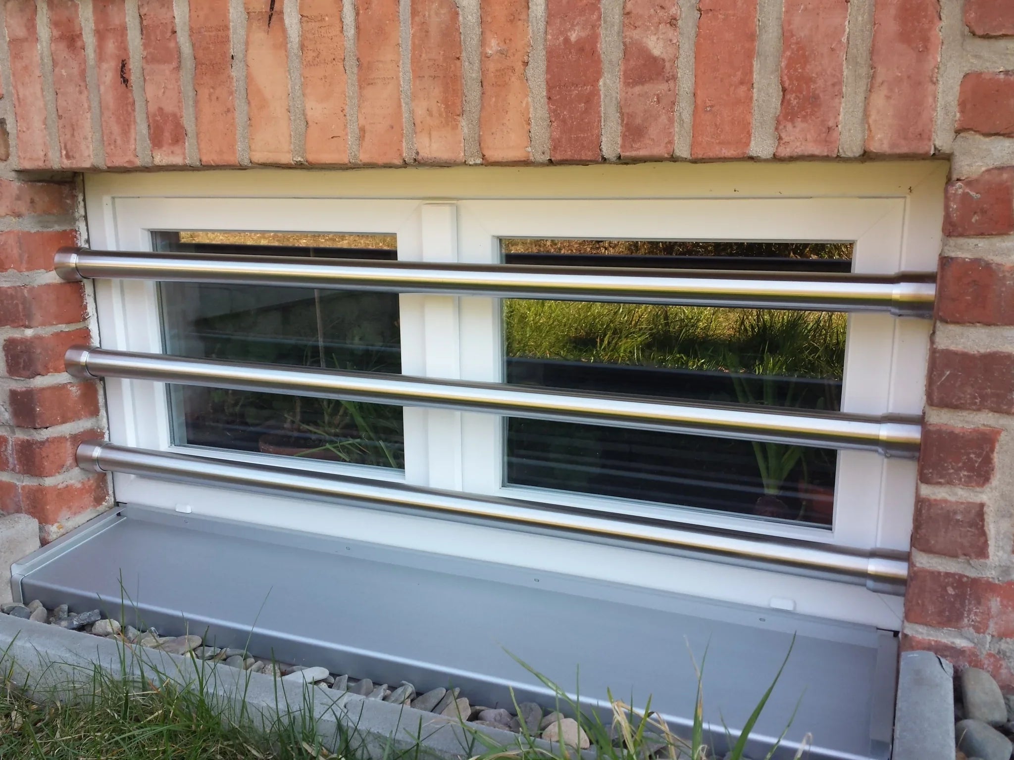 Fenstersicherung aus Edelstahl mit drei Stangen vor einem Kellerfenster in Backsteinwand