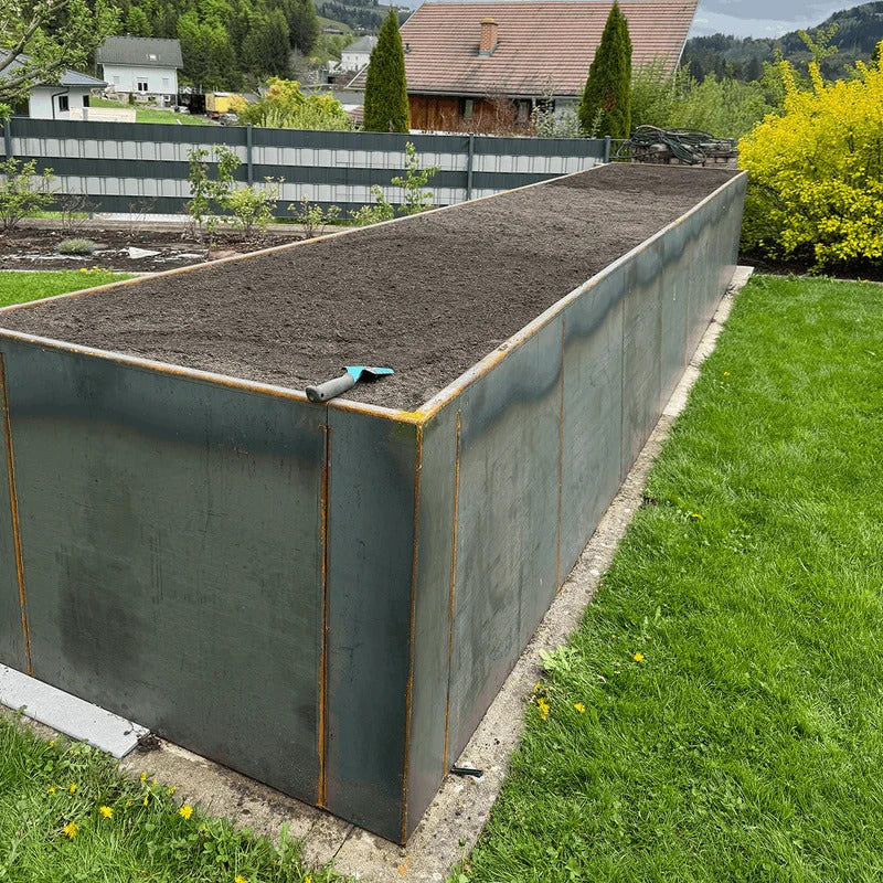 Kundenfoto: großes Cortenstahl Hochbeet nach Maß im Garten, frisch mit Erde befüllt, beginnende Edelrost-Patina an den Kanten