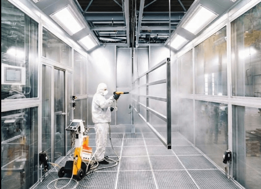 Pulverbeschichtung von Metallbauteilen in moderner Fertigungshalle, Mitarbeiter mit Schutzanzug
