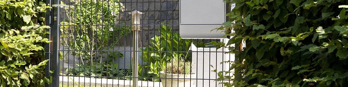 Einflügeliges Gartentor aus Metall mit schlichten Stabdesign, seitlich von Hecken umgeben
