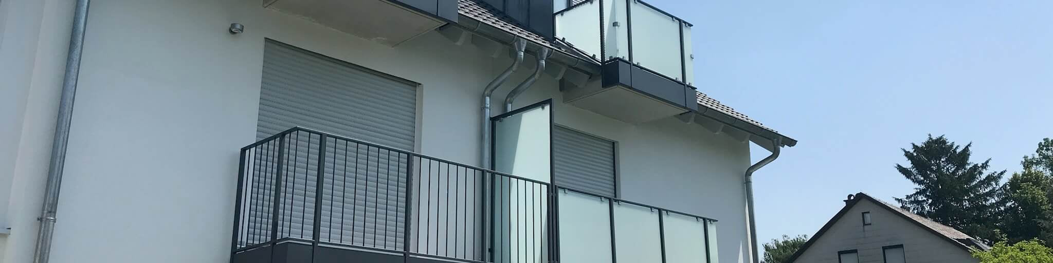 Modernes Haus mit Balkon und Glasgeländer, gepflegter Garten, sonniger Tag