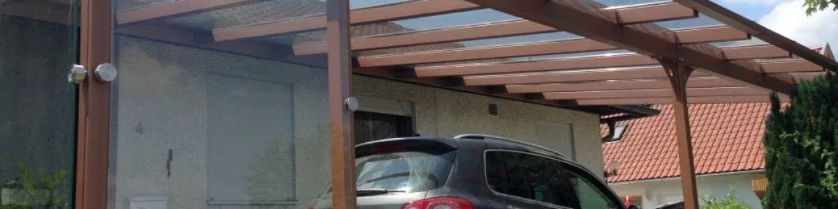 Modernes Carport aus Metall und Glas mit geparktem SUV vor einem Wohnhaus, wetterfest überdacht.