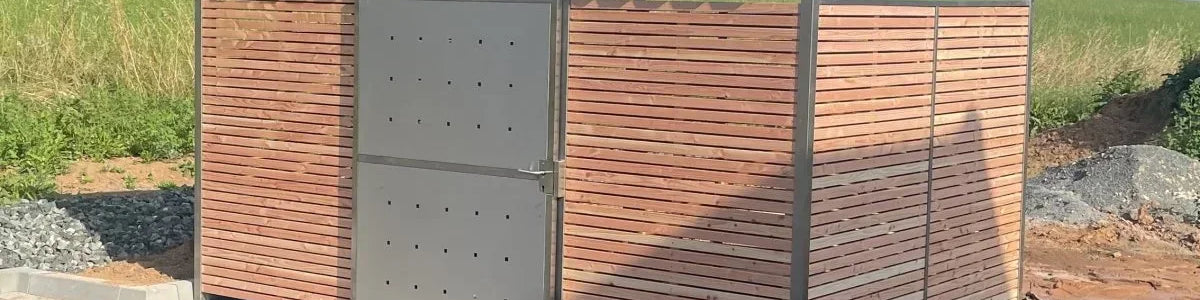 Modernes Mülltonnenhaus aus Metall und Holzlatten mit Flachdach auf gepflastertem Hof