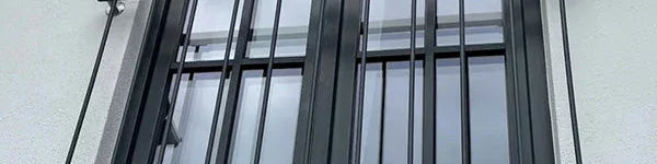 Französischer Balkon aus Metall vor modernem Fenster mit schwarzen Sprossen, Wandmontage