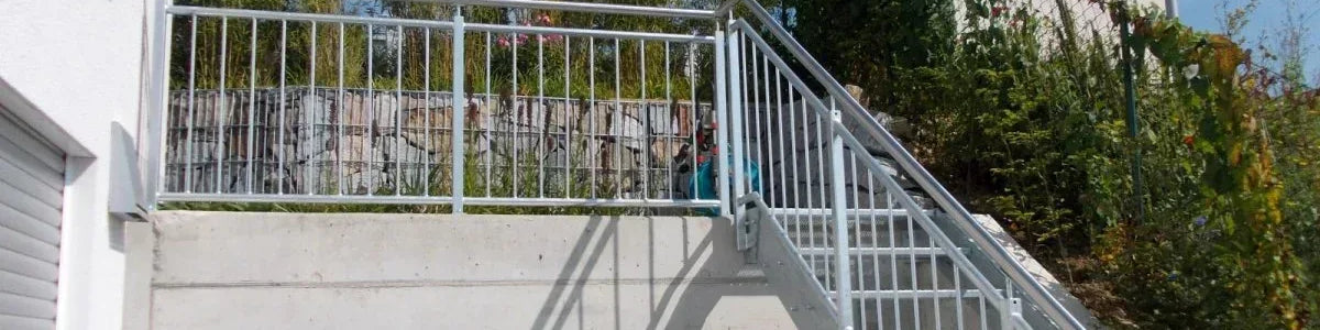 Außentreppe aus Metall mit Geländer an moderner Hauswand, Garten im Hintergrund