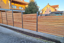Moderner Gartenzaun mit Holzlatten und Alu-Pfosten auf Betonmauer vor Wohnhaus
