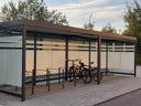 Überdachte Fahrradunterstand aus Metall mit Glaswänden und Fahrradständern im Außenbereich