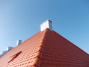 Steildach mit roten Dachziegeln und mehreren Blechdachaufbauten am klaren Himmel