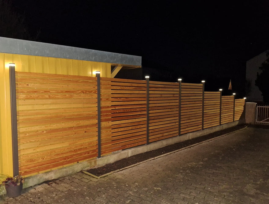Moderner Holz-Alu-Zaun mit integrierter LED-Beleuchtung bei Nacht an Einfahrt