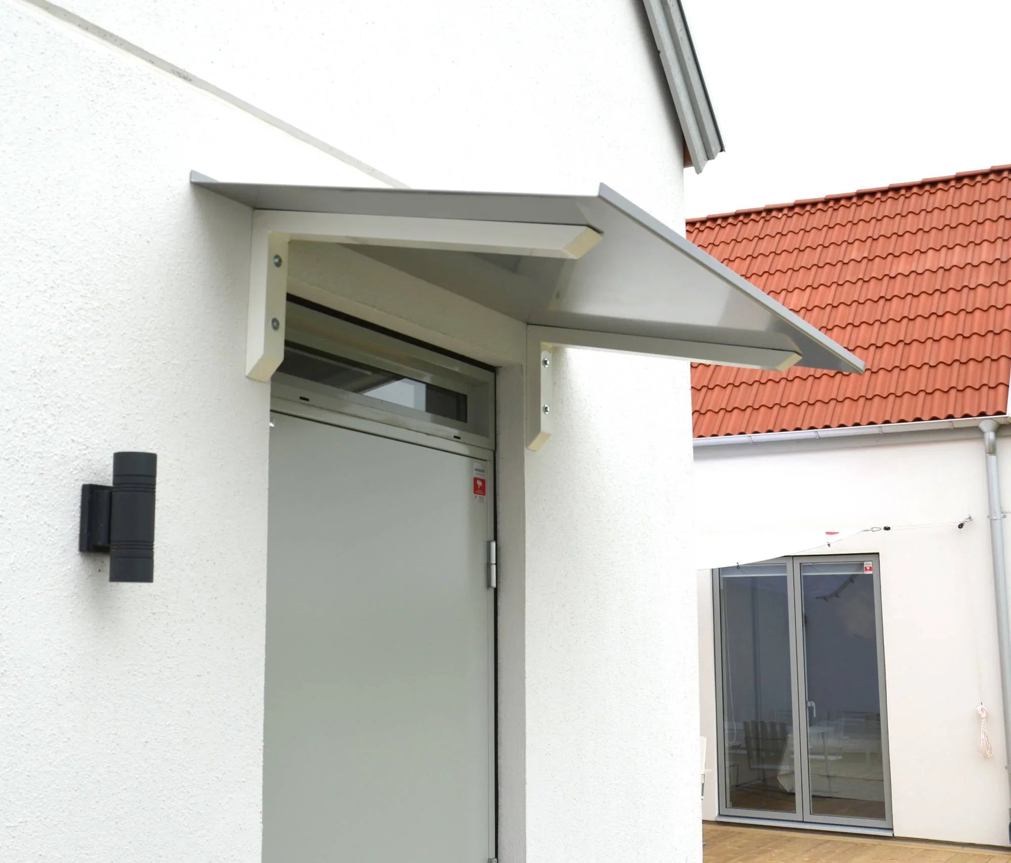 Modernes Vordach aus Aluminium in Silber mit weißen Wandkonsolen, montiert über einer Haustür