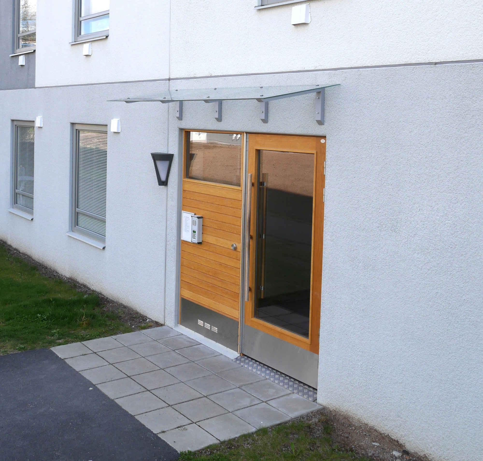 Vordach aus Klarglas mit silbernen Konsolen über einer modernen Hauseingangstür