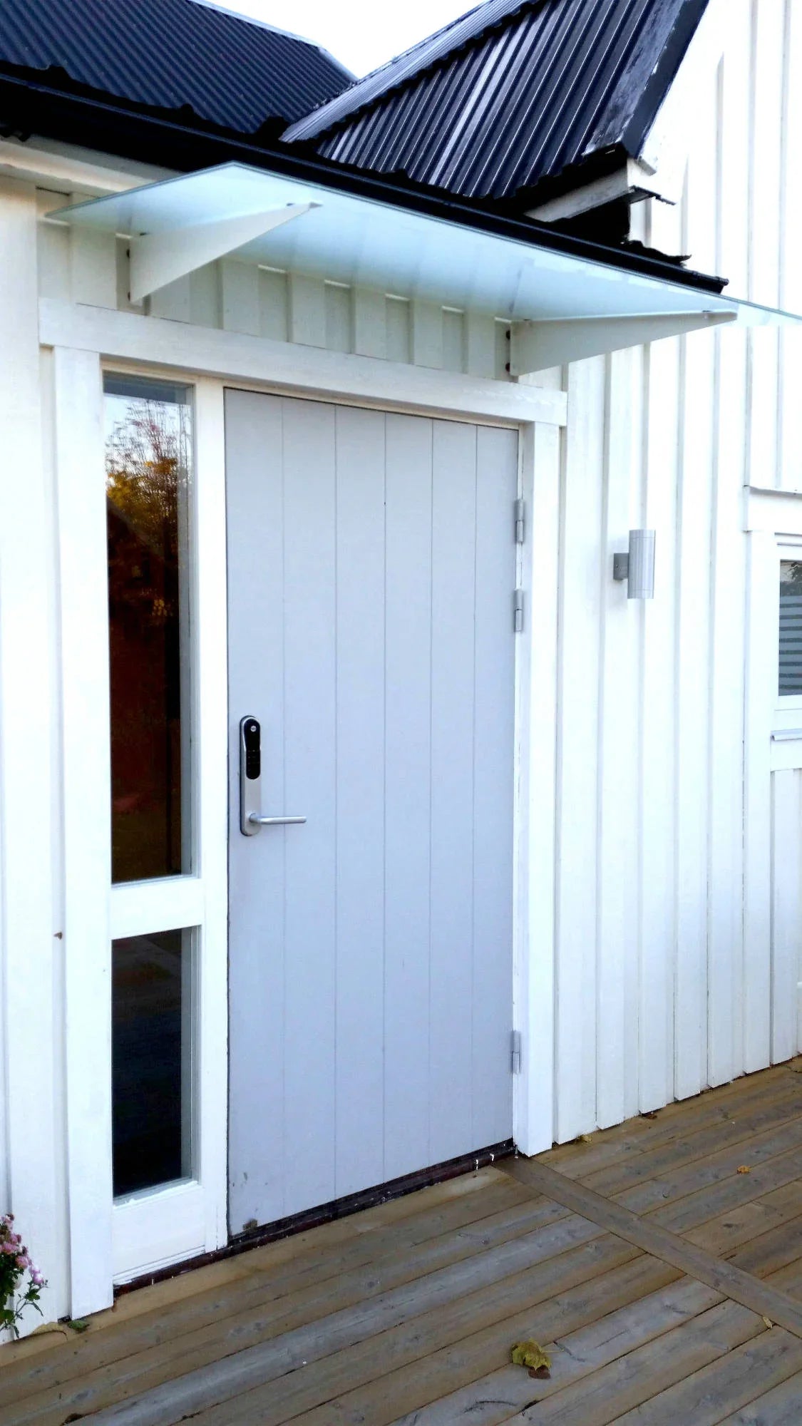 Vordach aus Milchglas mit weißen Wandkonsolen über moderner Haustür an weißem Haus