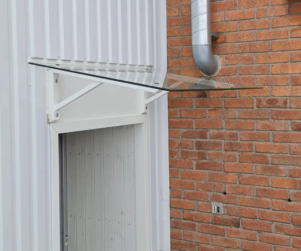 Vordach aus Klarglas mit weißen Metallkonsolen an Fassade, moderner Wetterschutz für Außentüren