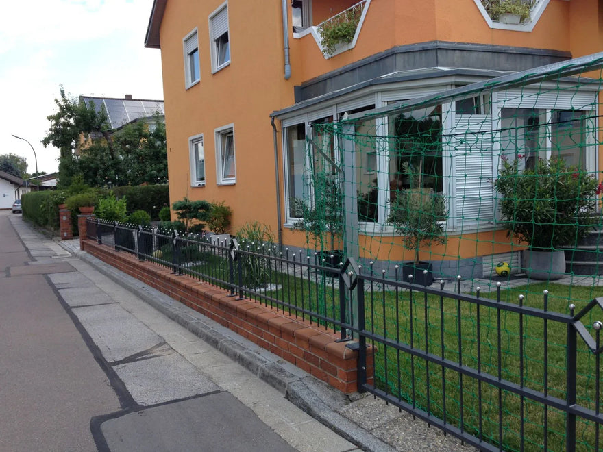 Moderner Metallzaun mit Zierspitzen auf Backsteinmauer vor Einfamilienhaus mit Garten