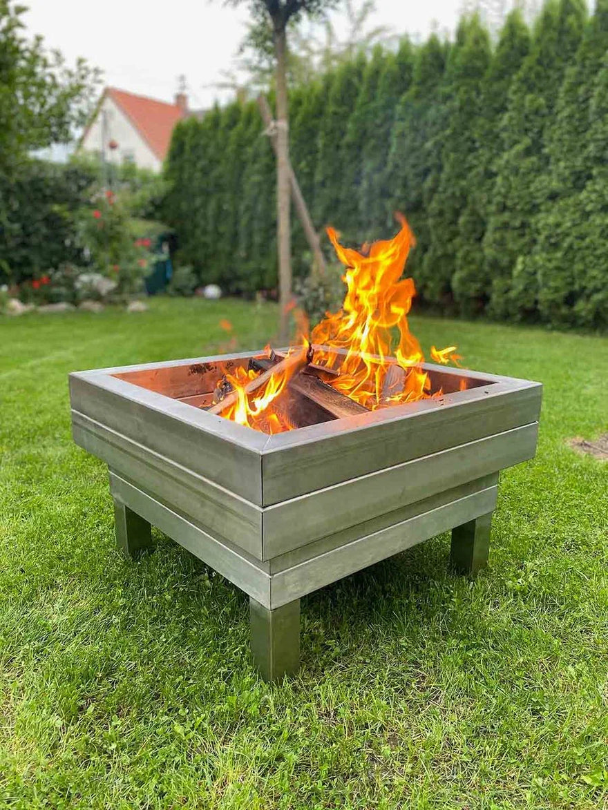 Moderne Edelstahl Feuerschale mit Flammen im Garten auf Rasen, eckiges Design