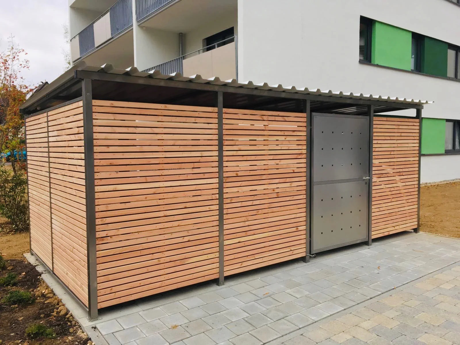 Moderne Fahrradgarage aus Metall und Holz mit Überdachung, vor Wohngebäude aufgestellt