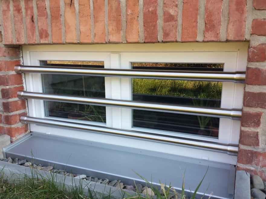 Fenstersicherung aus Edelstahl mit drei Stangen vor einem Kellerfenster in Backsteinwand