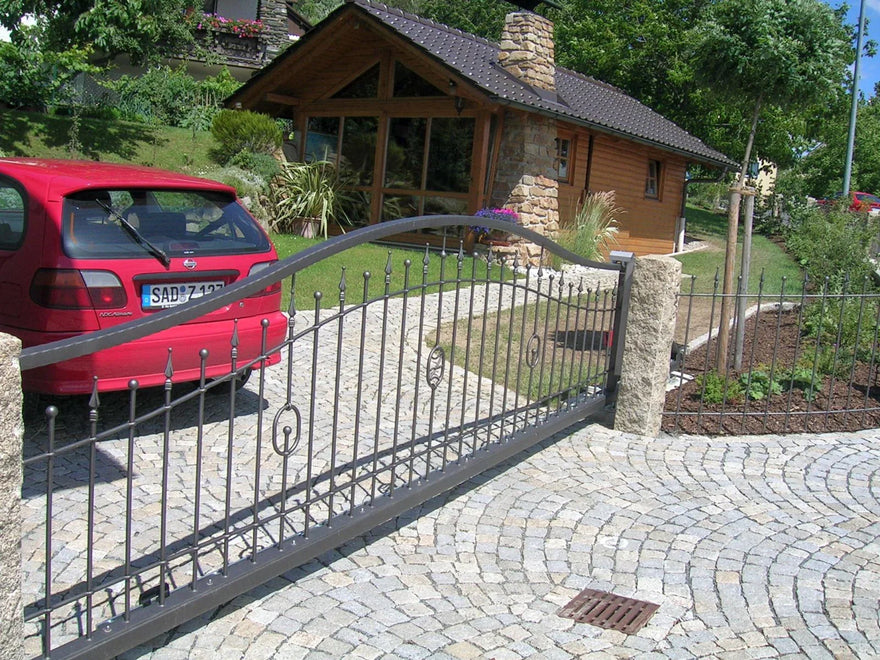Modernes schmiedeeisernes Hoftor vor Einfahrt mit Kopfsteinpflaster und Gartenhaus