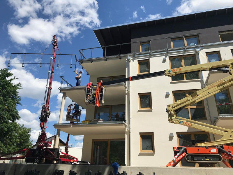 Montageteam setzt Balkongeländer mit Kran und Hebebühnen an einem Neubau ein