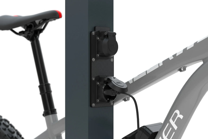 E-Bike Ladestation Detailansicht mit angeschlossenem Ladekabel und Fahrrad im Hintergrund