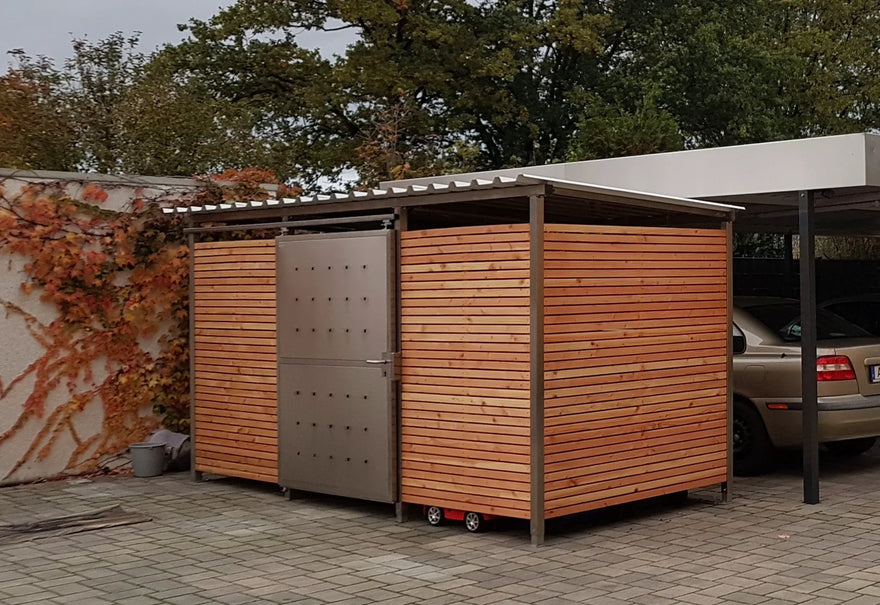 Modernes Mülltonnenhaus aus Edelstahl und Holz auf einem gepflasterten Parkplatz