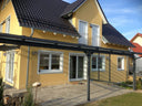 Moderne Terrassenüberdachung aus Metall an gelbem Einfamilienhaus auf Steinboden