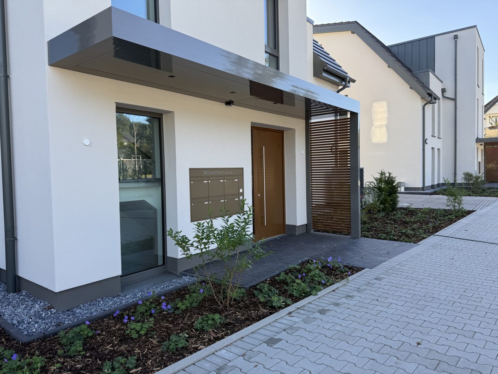 Aluminium-Vordach Platin auf Tragwerk in Anthrazit über einer Haustür, seitlich mit Lamellen-Sichtschutz